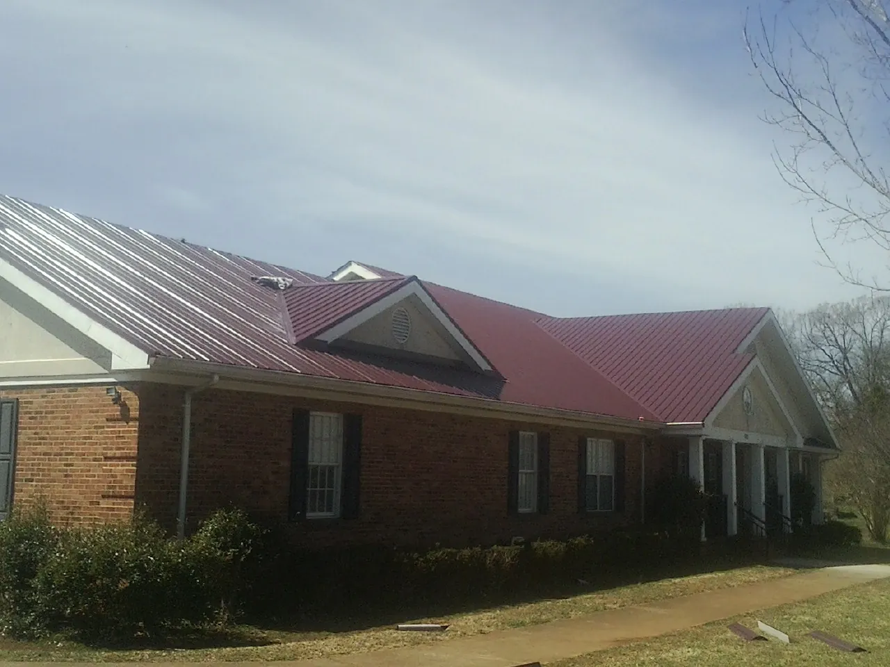 Red metal roof with gabled entries on a long brick building, from a Hail Damage Roof Repair job in Hazlehurst