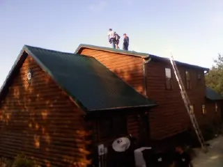 Crew on the ridge of a green metal roof on a two story log home in Hazlehurst