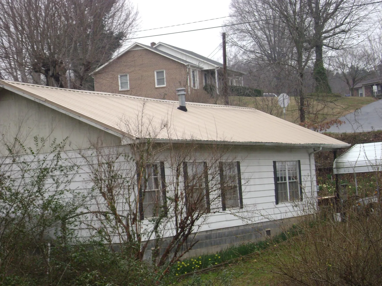 Tan metal roof on a white sided house set into a hillside — Commercial Roofing by Roofing Brothers in Hazlehurst