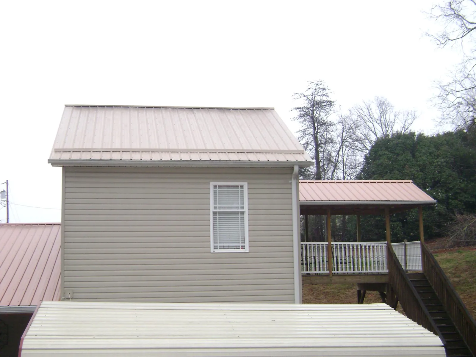 Tan metal roofs on a two story addition and attached porch, from a Roof Replacement job in Hazlehurst